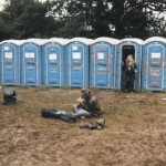 An excellent hippy having a psychedelic freakout with his guitar and amp in the mud by the toilets.
